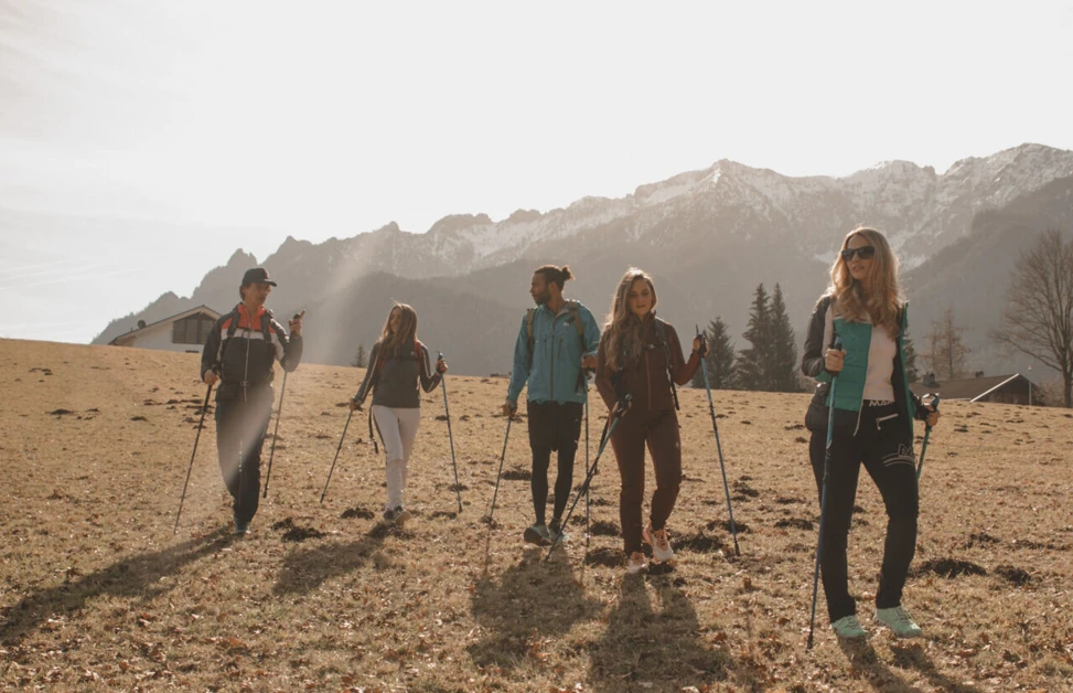 Group of people hiking with poles on a sunny day with mountains in the background.