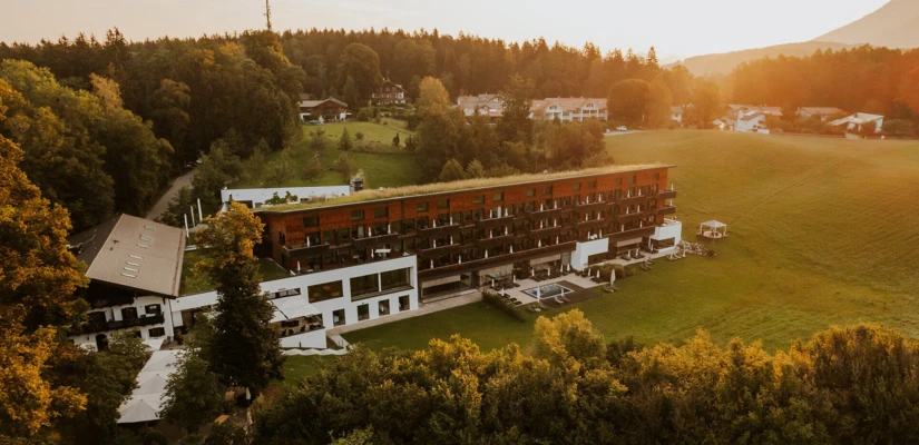 Ein modernes Hotelgebäude inmitten von Bäumen und Wiesen, bei Sonnenuntergang, umgeben von einer idyllischen Landschaft.