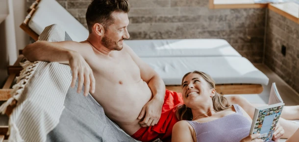 Ein Paar entspannt sich auf einer Liege im Klosterhof, während sie gemeinsam lächeln und ein Buch lesen.