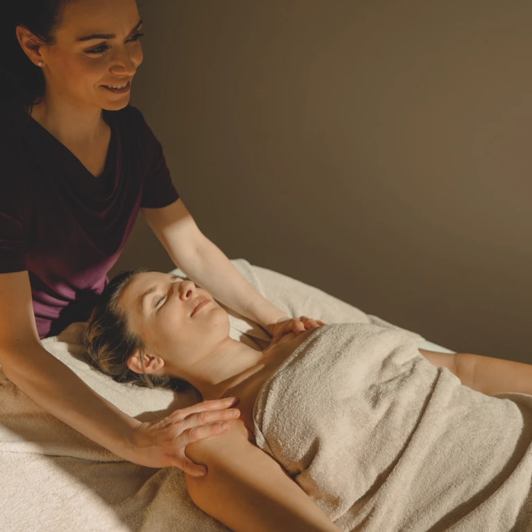 Eine Therapeutin bietet eine Massage in einem Wellnesshotel an, während eine entspannte Frau auf der Liege liegt.