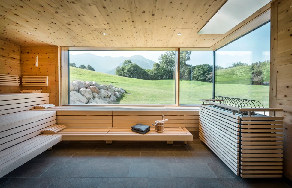 Modernes Sauna-Interieur mit Holzdetails und Blick auf die gr&uuml;ne Landschaft und Berge durch gro&szlig;e Fenster. Entspannung pur.