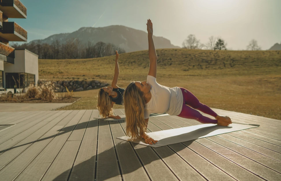 Two people practicing yoga on a deck with mountains in the background.