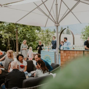 Menschen genie&szlig;en eine entspannte Zeit im Freien unter einem gro&szlig;en Sonnenschirm, w&auml;hrend ein Barkeeper Cocktails zubereitet.