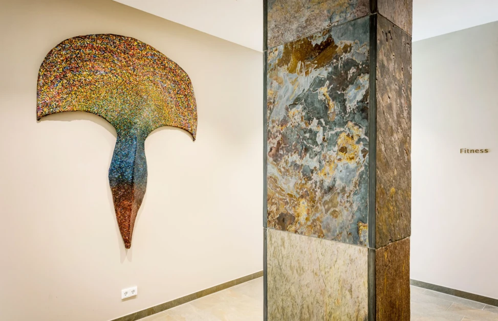 Colorful abstract wall art next to a stone pillar in the Wellnesshotel Klosterhof in Bayern. "Fitness" sign visible on the wall.