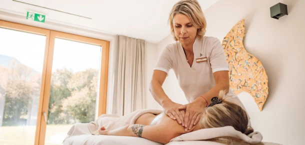 Eine Masseurin führt eine entspannende Massage in einem hellen Wellnessraum durch, umgeben von natürlichem Licht und beruhigender Atmosphäre.
