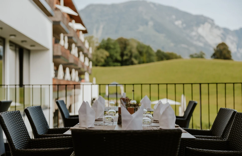 Outdoor dining area with set table, wicker chairs, and mountain view at a hotel.