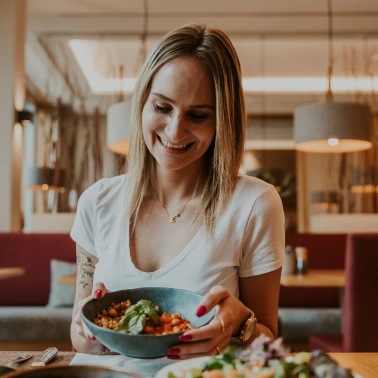 A woman smiling while holding a bowl of food in a cozy restaurant setting.