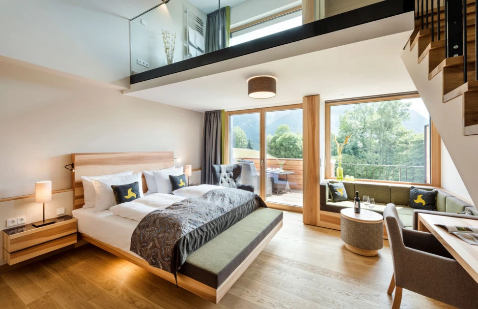 Modern hotel room with a loft, featuring a large bed, seating area, and balcony with mountain views at Hotel Klosterhof.