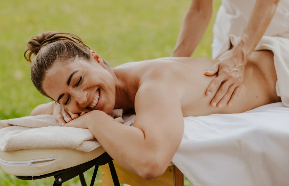A woman enjoys a relaxing outdoor massage on a table, smiling with eyes closed.