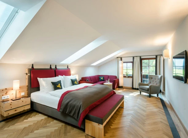 Spacious hotel room with elegant decor, featuring a large bed, cozy seating area, and natural light from skylights and windows.