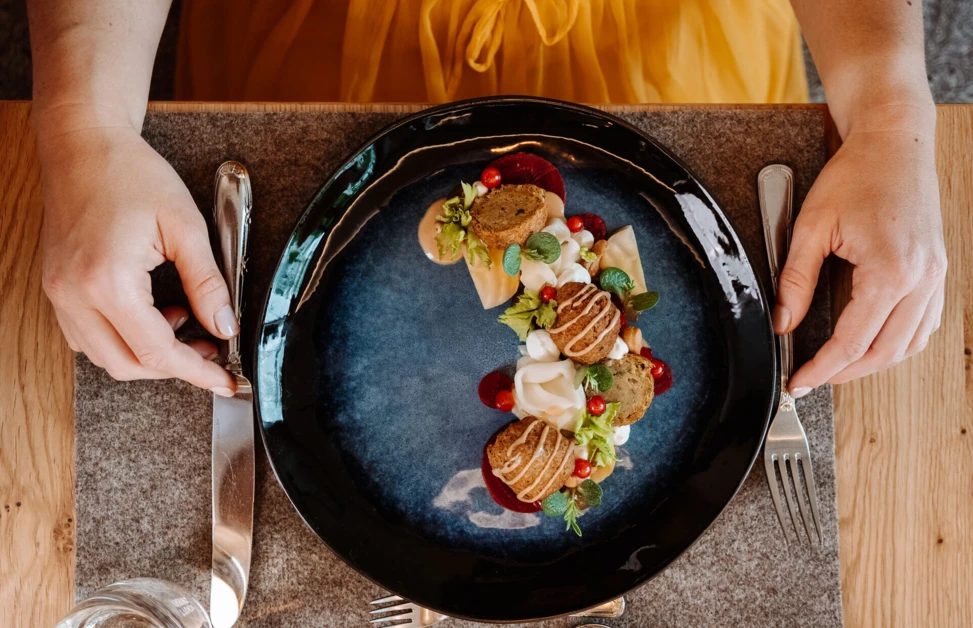 A gourmet dish elegantly presented on a dark plate, with vibrant garnishes, on a wooden table setting.