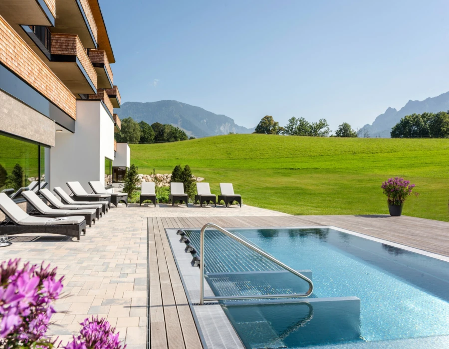 Ein moderner Außenbereich des Hotel Klosterhof mit Liegen und einem Pool, umgeben von grünen Wiesen und Bergen in Bayerisch Gmain.