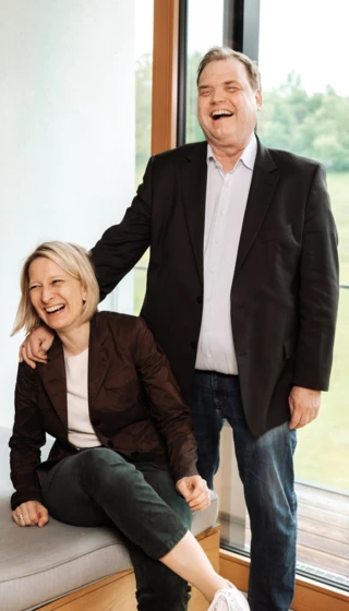 Lächelnde Personen in einem modernen Raum, die Freude und Freundschaft ausstrahlen, mit Blick auf eine grüne Landschaft.