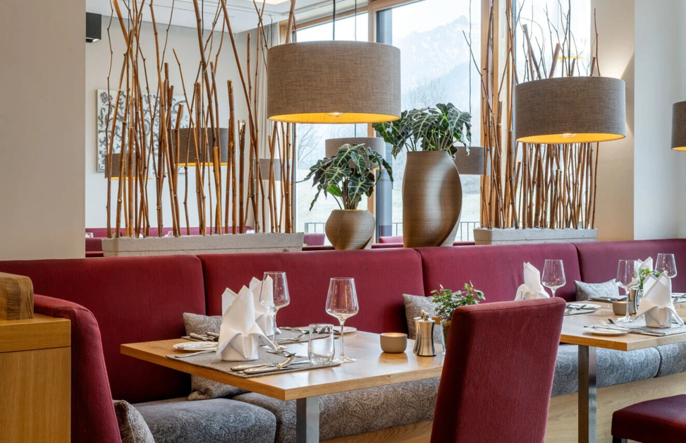 Gemütliche Restaurantatmosphäre im Hotel Klosterhof mit roten Sitzbänken, eleganten Tischen und Blick auf die bayerischen Alpen.