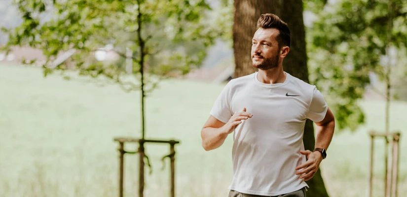 Ein junger Mann joggt auf einem Weg durch eine grüne Landschaft, umgeben von Bäumen und natürlicher Schönheit.