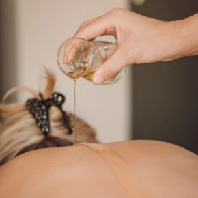 Eine Hand gießt Massageöl auf den Rücken einer Person in einem entspannenden Wellnessumfeld.