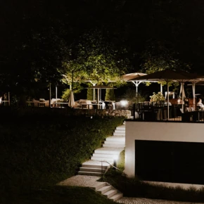 Nachtszene im Gartenrestaurant des Hotel Klosterhofs mit beleuchteten Tischen unter Sonnenschirmen.