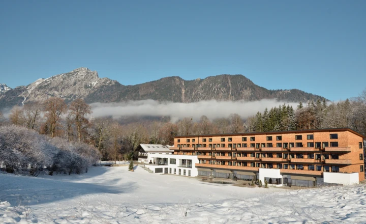 Hotel in winterlicher Landschaft, umgeben von schneebedeckten Bäumen und Bergen.