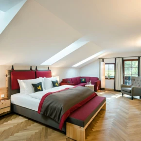 Helles, modernes Zimmer im Hotel Klosterhof mit zwei Betten, gemütlicher Sitzecke und Blick auf die Alpen. Ideal für Wellness und Entspannung.