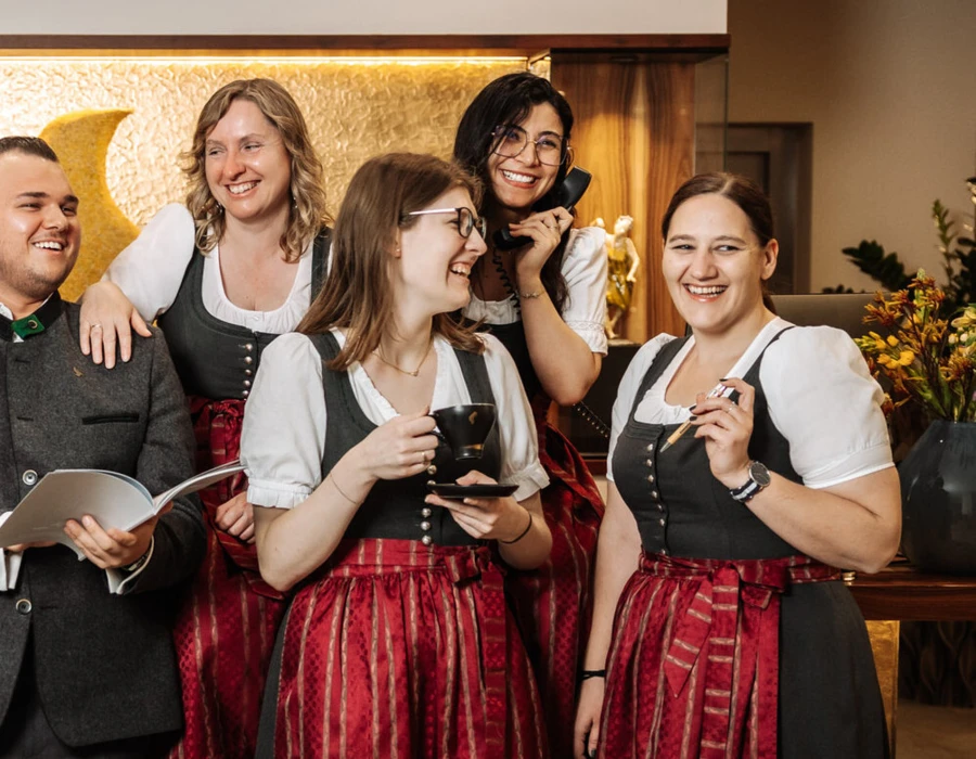 Gruppenfoto von Mitarbeitern in traditioneller Tracht, lächelnd und fröhlich in einer Empfangshalle mit Blumenarrangements.