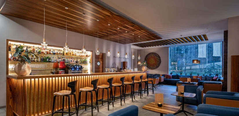 Modern bar area with wooden accents and cozy seating at Wellnesshotel Klosterhof in Bayern, featuring a well-stocked bar and ambient lighting.