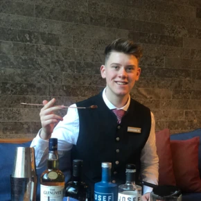 Ein Barkeeper präsentiert verschiedene Spirituosen und Cocktail-Utensilien in einem modernen Ambiente im Hotel Klosterhof.