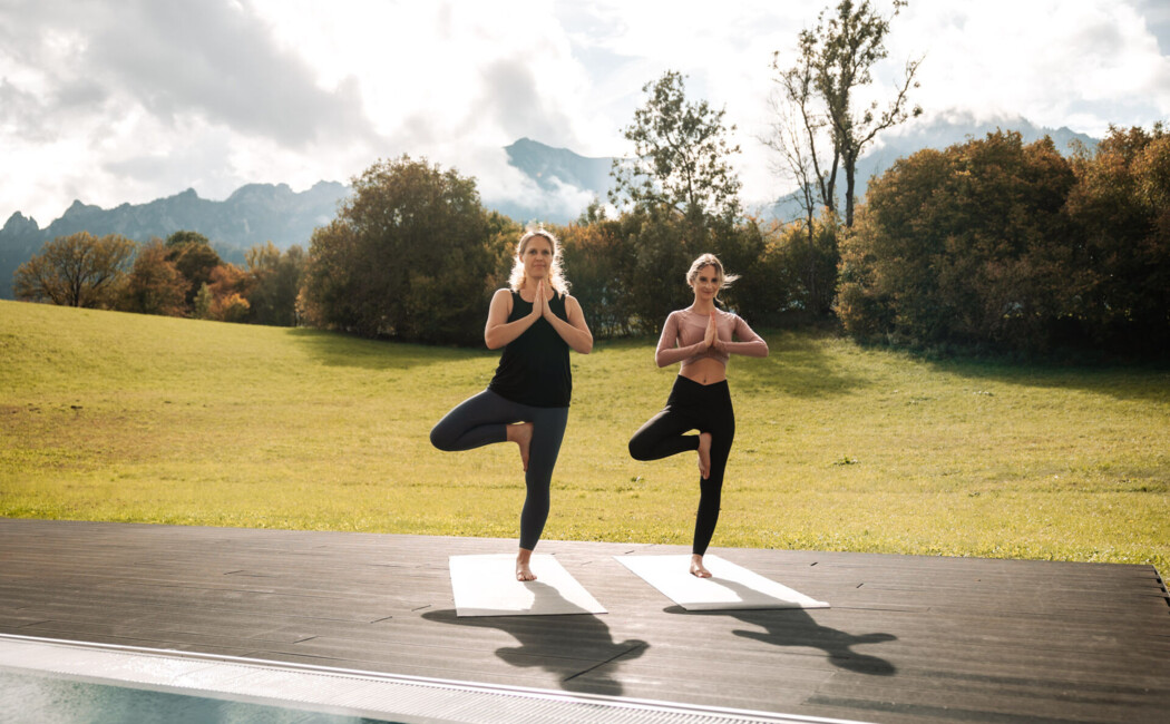 Zwei junge Frauen bei Yoga-Übung am Außenpool des Wellnesshotels Klosterhof im Berchtesgadener Land.