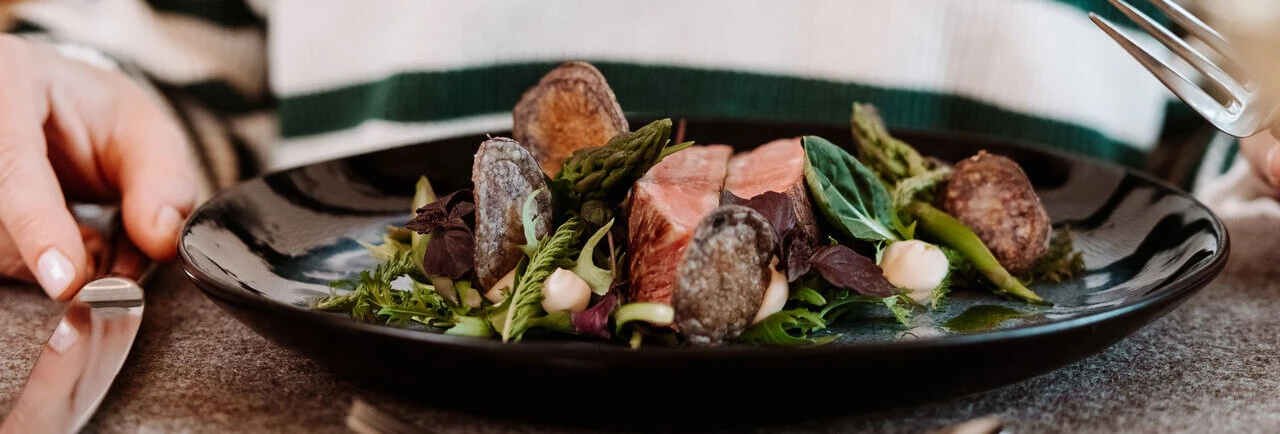 Eine Person sitzt am Tisch mit einem Teller voller frischem Gemüse und Fleisch, bereit zum Essen in einem gemütlichen Ambiente.