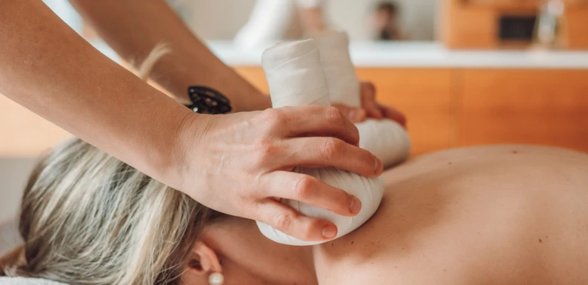 Eine Person erhält eine wohltuende Massage mit heißen Kräuterstempeln in einem Wellnessbereich. Entspannung und Erholung im Hotel Klosterhof.