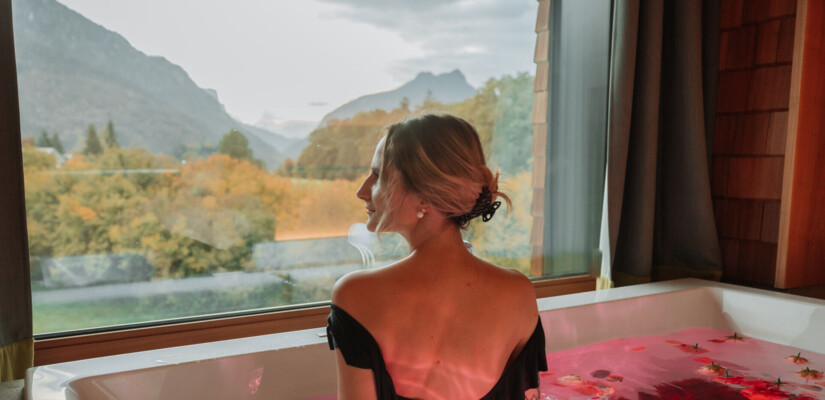 Junge Dame im Whirlpool mit Rosenblättern und Blick aus dem Panoramafenster im Hotel Klosterhof, Bayern.