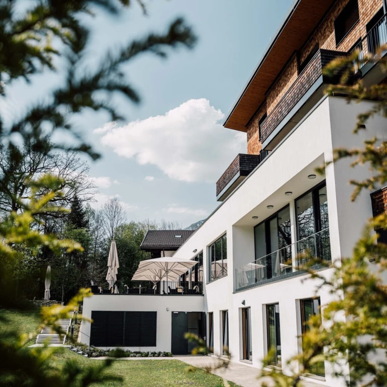 Modern hotel building with terraces and umbrellas, surrounded by greenery, under a blue sky at Hotel Klosterhof.