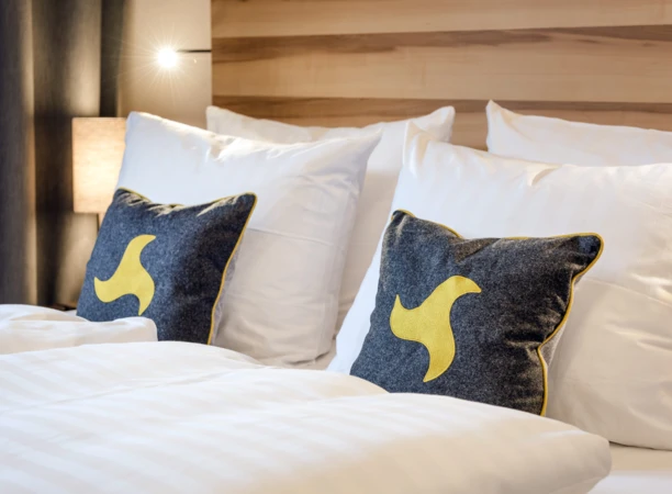 Cozy hotel bed with white linens and decorative pillows featuring yellow designs at Hotel Klosterhof.
