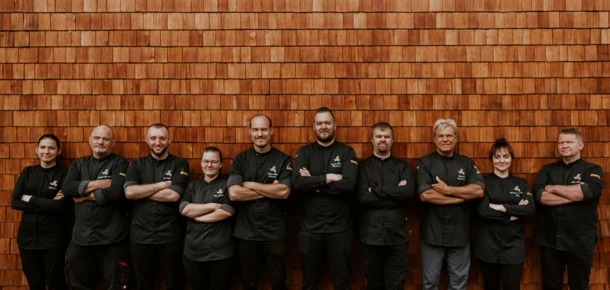 A group of chefs in black uniforms stands with arms crossed, posing in front of a wooden wall at Hotel Klosterhof.