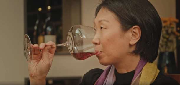 A person tasting red wine from a glass in a cozy setting.