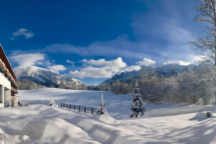 Schneebedeckte Landschaft mit Blick auf die Berge und das Hotel Klosterhof in Bayerisch Gmain. Helle, sonnige Atmosphäre.