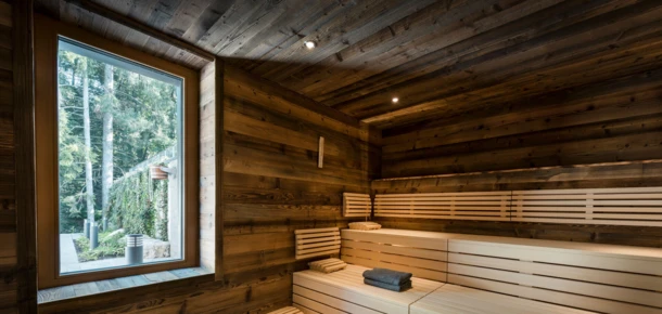 Modern wooden sauna with a window view of lush greenery outside.