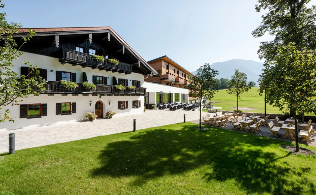 Ein malerisches Hotelgebäude mit traditioneller Architektur, umgeben von Grünflächen und gemütlichen Sitzgelegenheiten im Freien.