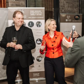 Ein fröhliches Event im Hotel Klosterhof mit Gästen, die anstoßen und sich unterhalten. Im Hintergrund sind Werbebanner sichtbar.