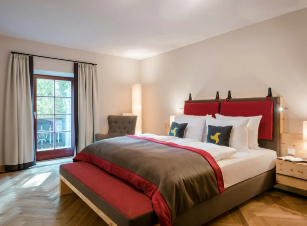Elegant hotel room with a large bed, red accents, and cozy lighting, featuring a window with a view.