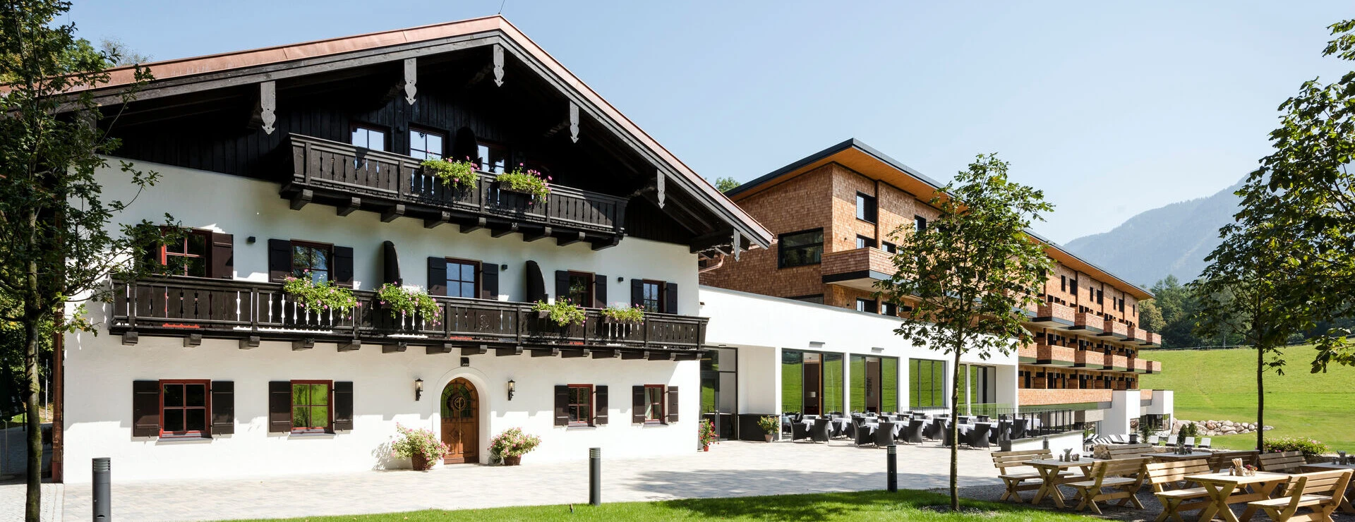 Charming hotel with traditional architecture, surrounded by lush greenery and mountains, featuring outdoor seating.