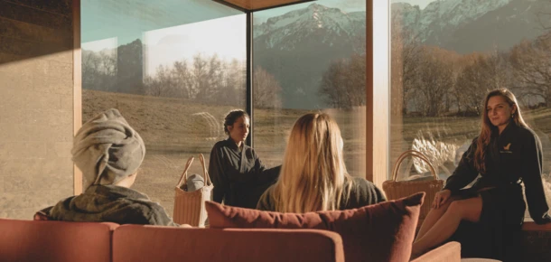 Entspannende Atmosphäre im Spa mit Gästen, die die Aussicht auf die Berge genießen. Moderne Einrichtung und natürliche Lichtverhältnisse.