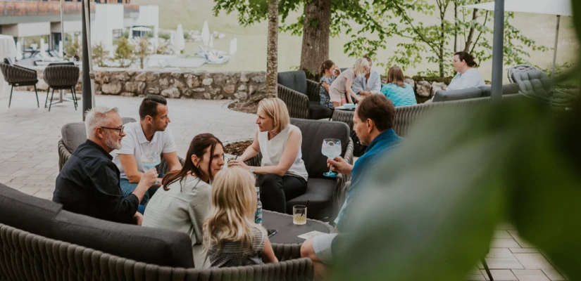 Gemütliche Runde von Gästen im Außenbereich des Hotel Klosterhof, umgeben von Bäumen und Sonnenschirmen.
