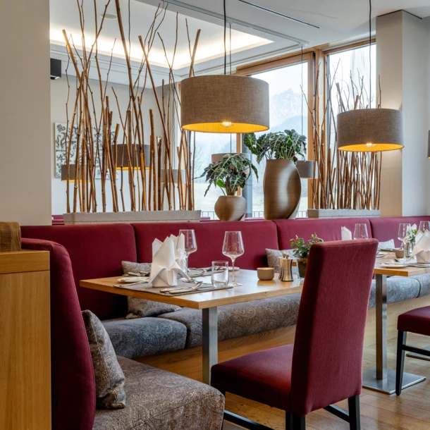 Ein modernes Restaurant mit roten Stühlen, Holztischen und großen Fenstern, die eine schöne Aussicht auf die Natur bieten.