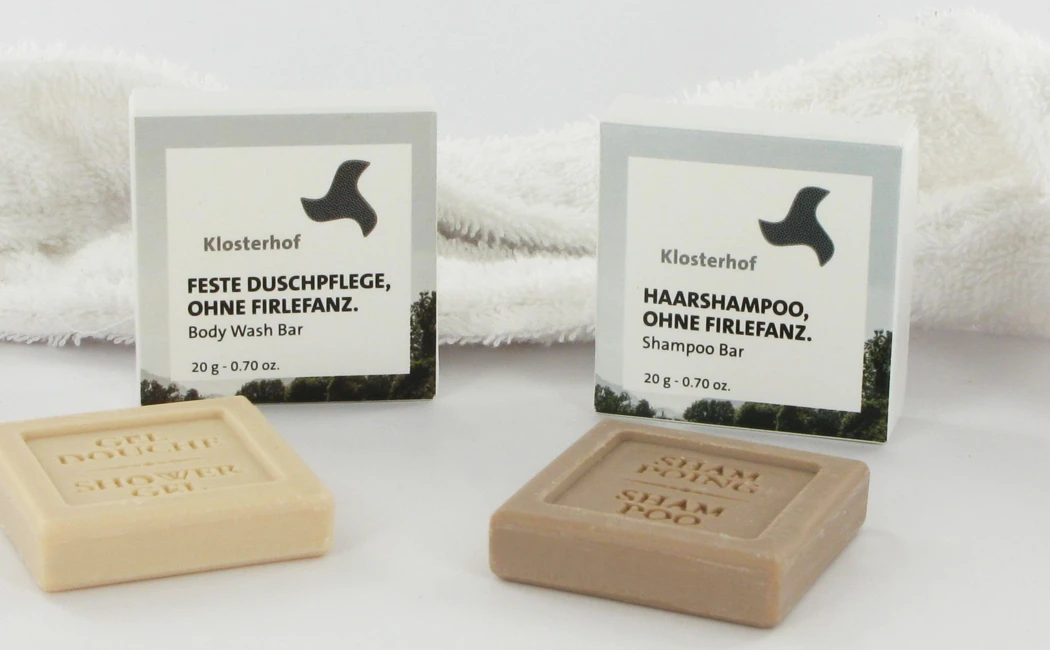 Zwei feste Pflegeprodukte von Klosterhof: ein K&ouml;rperwaschbar und ein Shampoo-Bar, pr&auml;sentiert auf einem wei&szlig;en Handtuch.