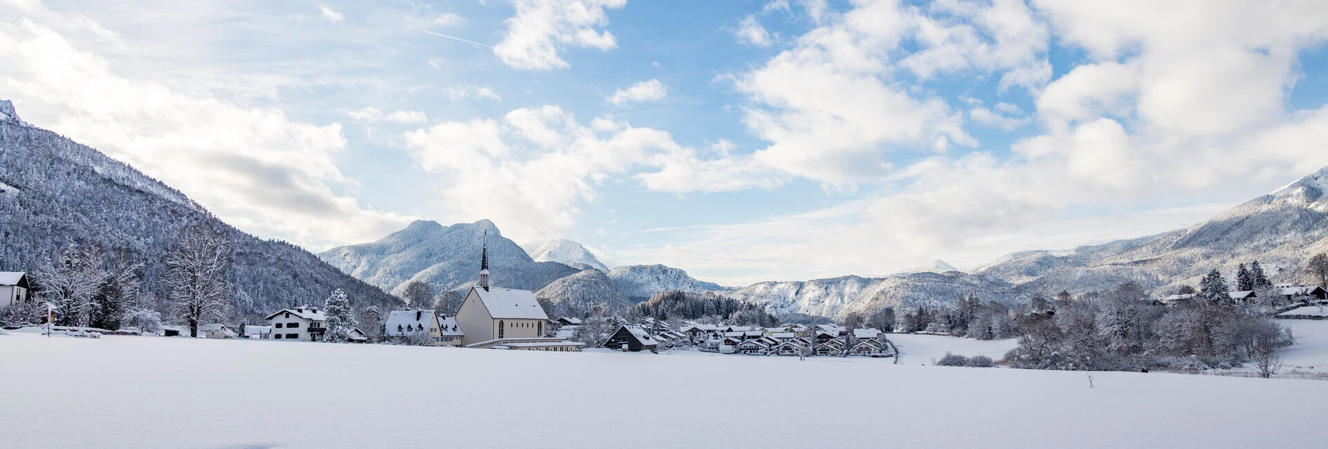 Schneebedeckte Landschaft mit einem Hotel im Vordergrund und Bergen im Hintergrund, gelegen in Bayerisch Gmain, Bayern.