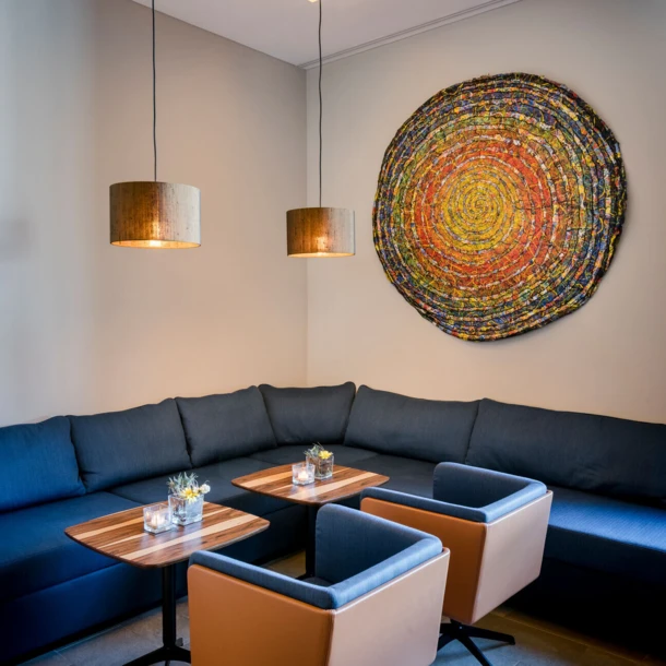 Gemütliche Lounge mit blauen Sofas, Holztischen und modernen Lampen. Bunte Wandkunst verleiht dem Raum eine lebendige Atmosphäre.