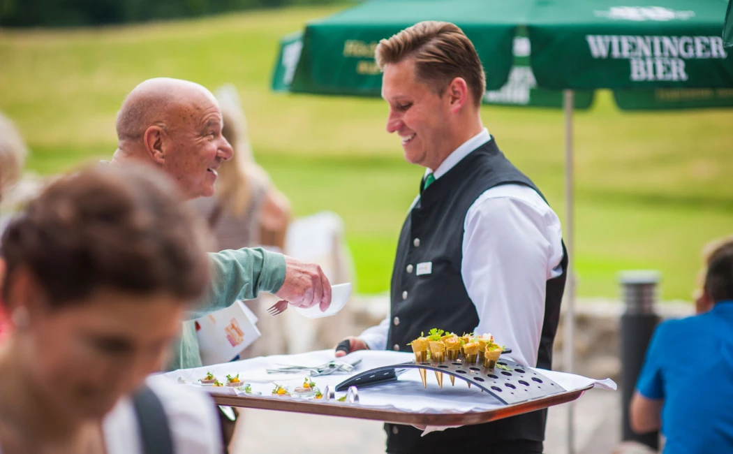Ein Kellner serviert Appetithäppchen an einen Gast im Hotel Klosterhof, umgeben von einer entspannten Atmosphäre im Freien.