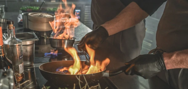 Chefs flambéing dishes in a professional kitchen at Hotel Klosterhof, showcasing culinary expertise and dynamic cooking techniques.