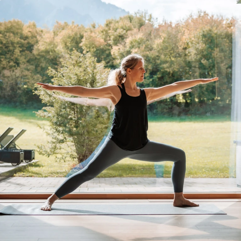 Eine Person praktiziert Yoga in einem modernen Raum mit großen Fenstern, die auf eine grüne Landschaft blicken.