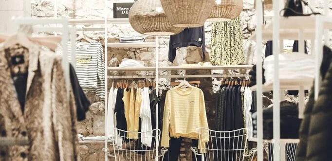 Ein stilvoll eingerichteter Bekleidungsladen mit geflochtenen Lampen und moderner Mode auf Kleiderständern.